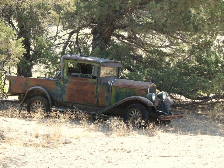 an old rusty truck in the field near a tree