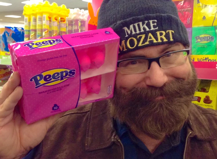 a man with glasses and a hat holding a package of peeps