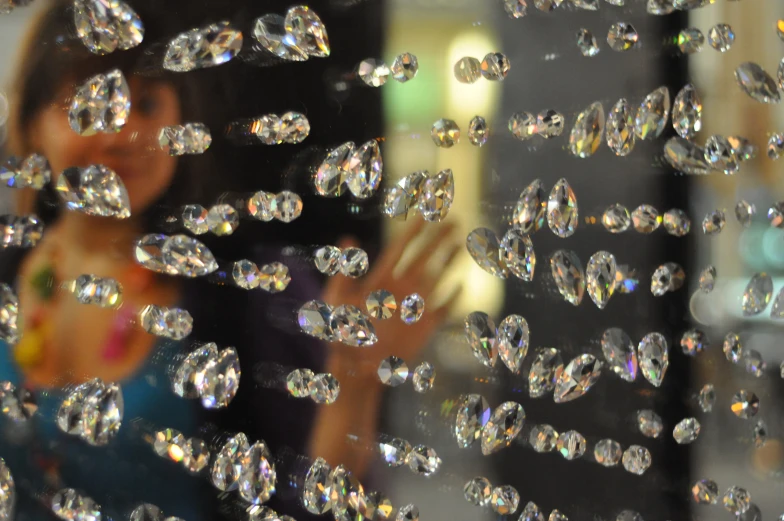 the young woman is smiling behind a window that contains crystals