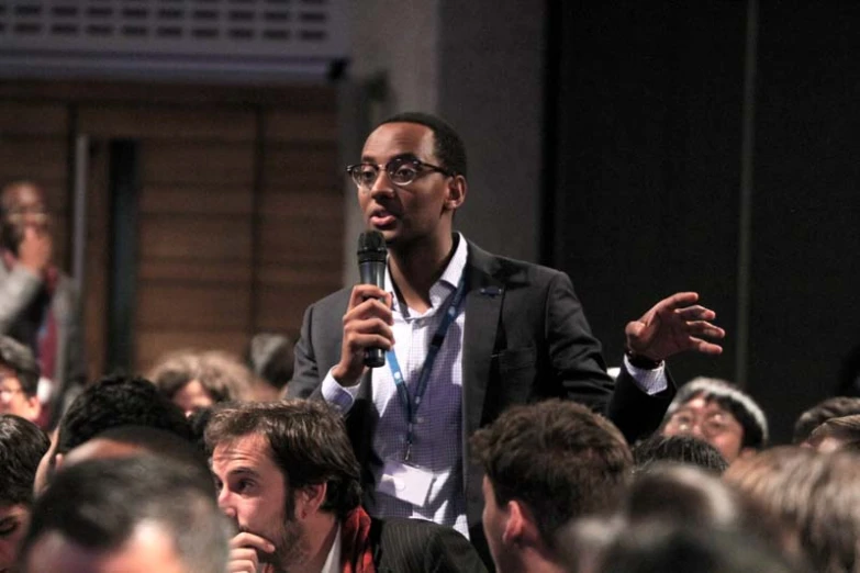 man in suit speaking into a microphone surrounded by people