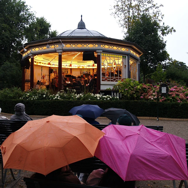 several people under open umbrellas on park benches