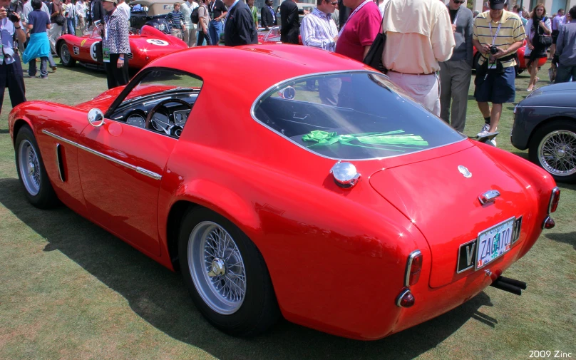 people are gathering and looking at an antique red car