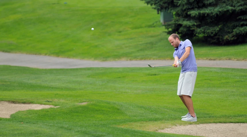 a male golfer in a blue shirt is swinging his club