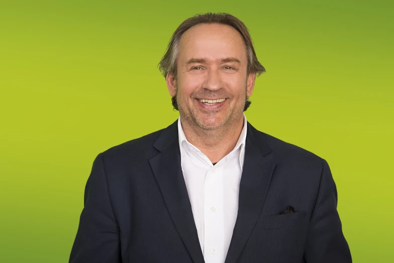 a man is smiling and standing against a green background