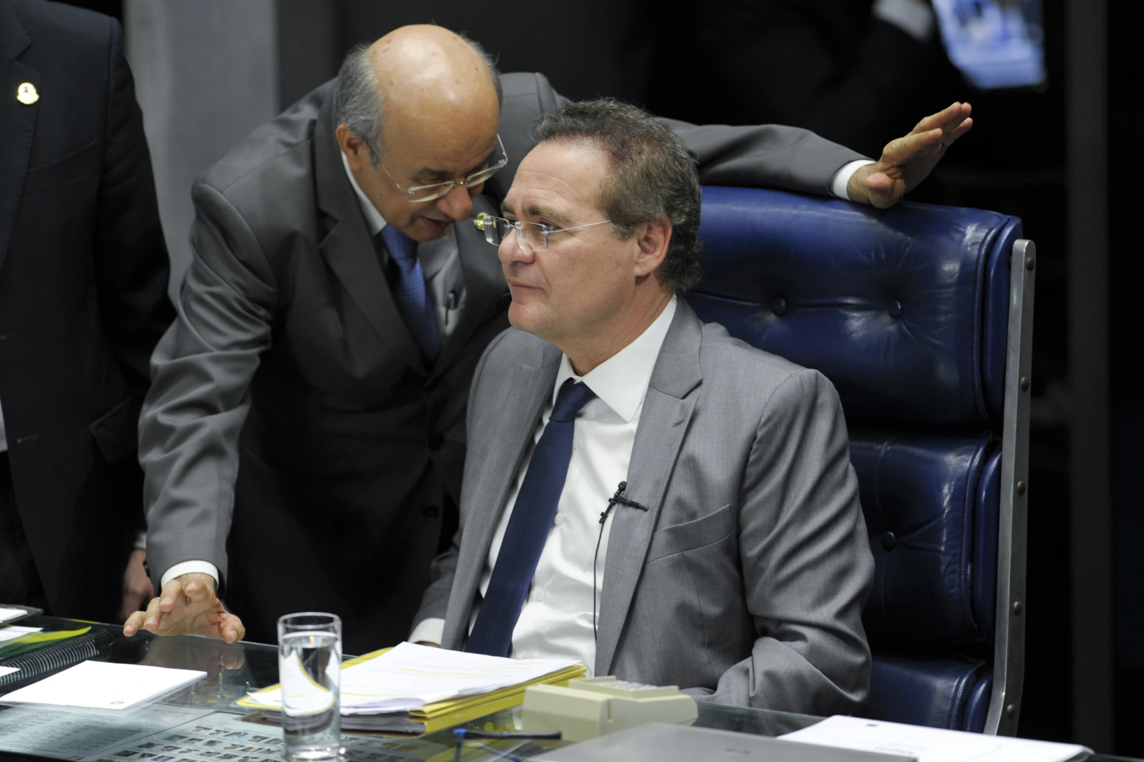 two men in suits and ties are looking at papers on a desk