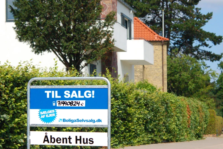 a blue sign with white lettering is in front of some bushes