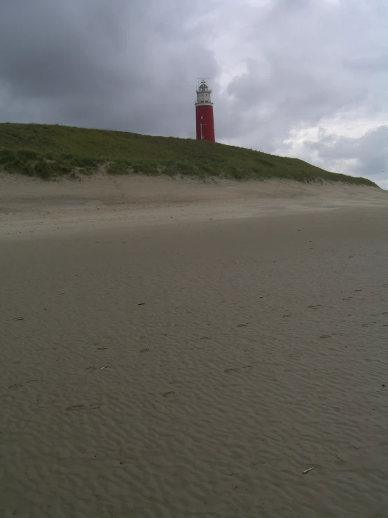 a red and white lighthouse sitting on top of a sandy hill
