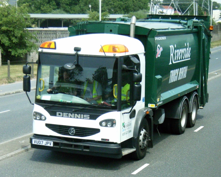 a large green garbage truck driving down a street