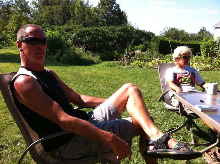 there are two men sitting at a table outside in the yard