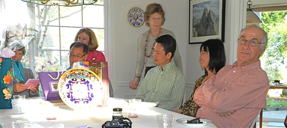 people standing and sitting at a table in a room with a plate on it