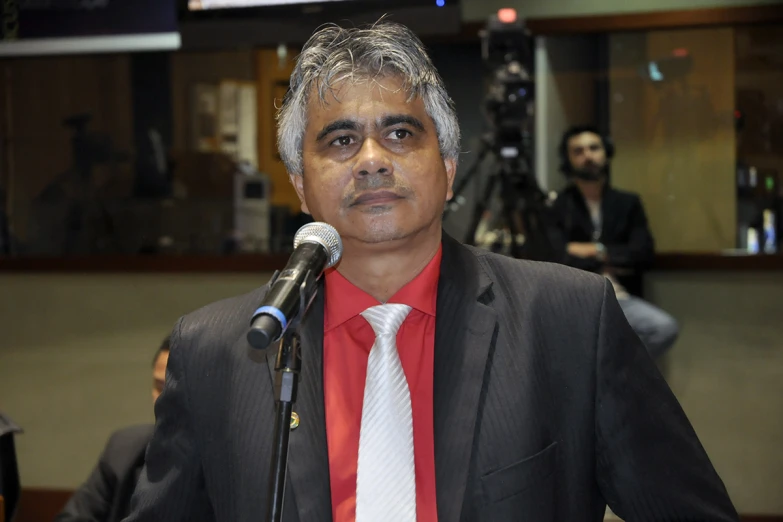 a man standing behind a microphone wearing a black suit