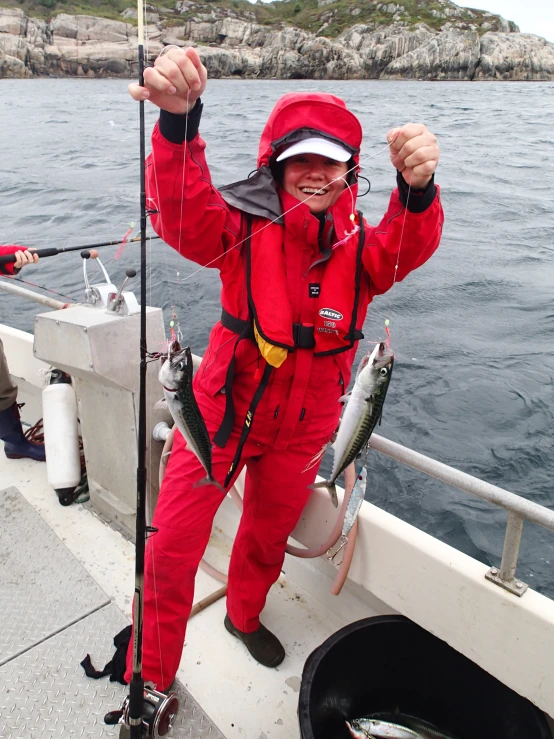 a man in red and black standing on the edge of a boat while holding onto two small fish