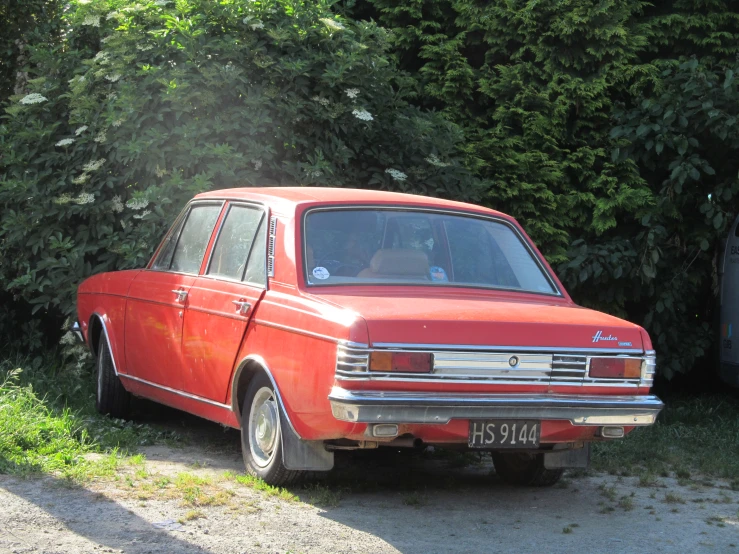 an old red car with trees behind it