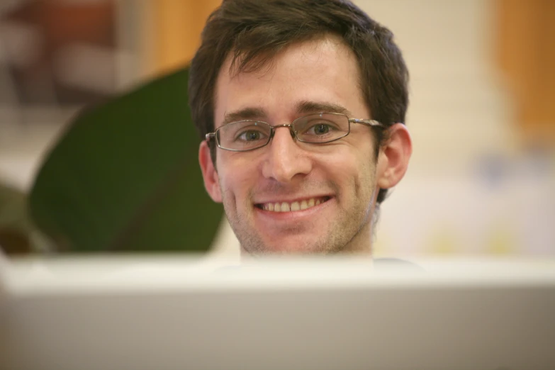 a man with glasses and eyeglasses smiling in front of a laptop