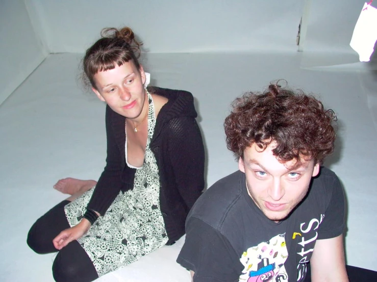 a girl with brown curly hair sitting on the floor next to a guy