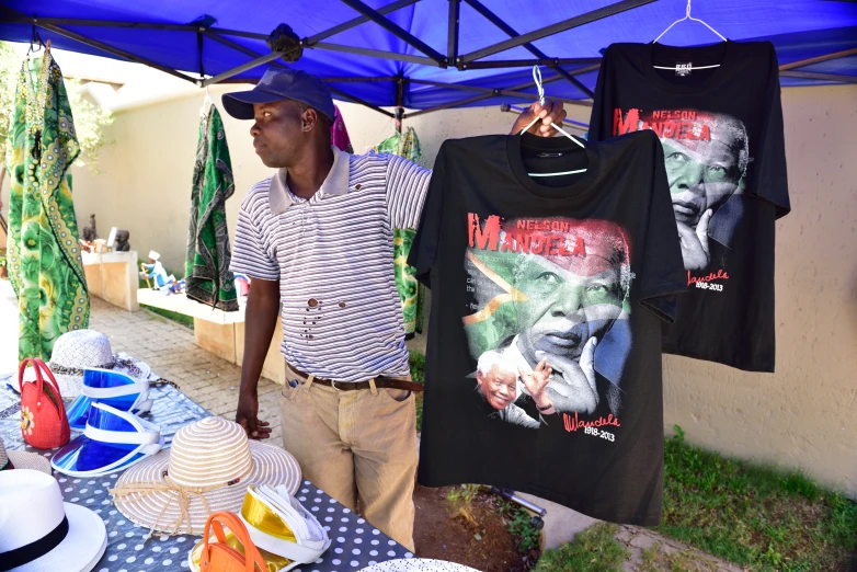 a man stands under an umbrella selling t - shirts