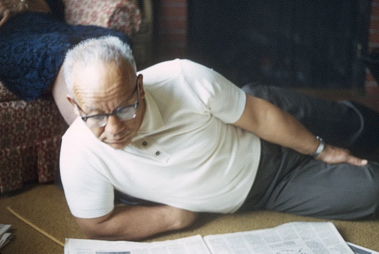 the man is reading his newspaper while lying on the floor