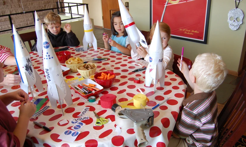 four children sitting at a red table with white and blue cones on it
