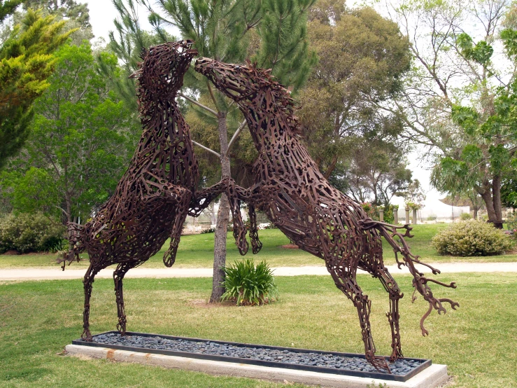 two giraffe sculptures made from old nches are in a park