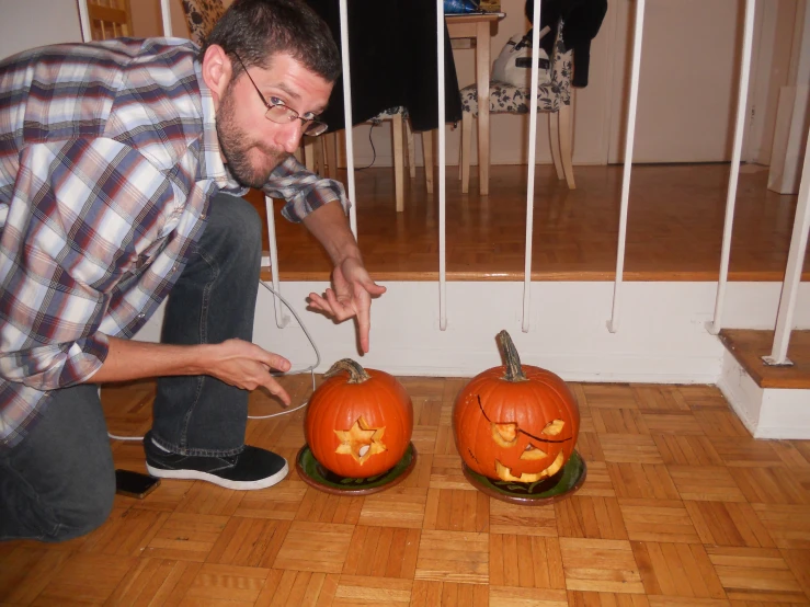 man standing by two pumpkin shaped carvings, one with carving eyes