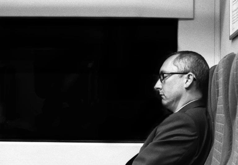 a man with glasses sitting next to a window