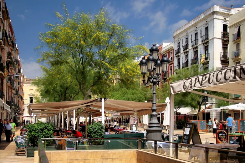 a street scene showing people sitting and walking, in the middle of a tree lined area