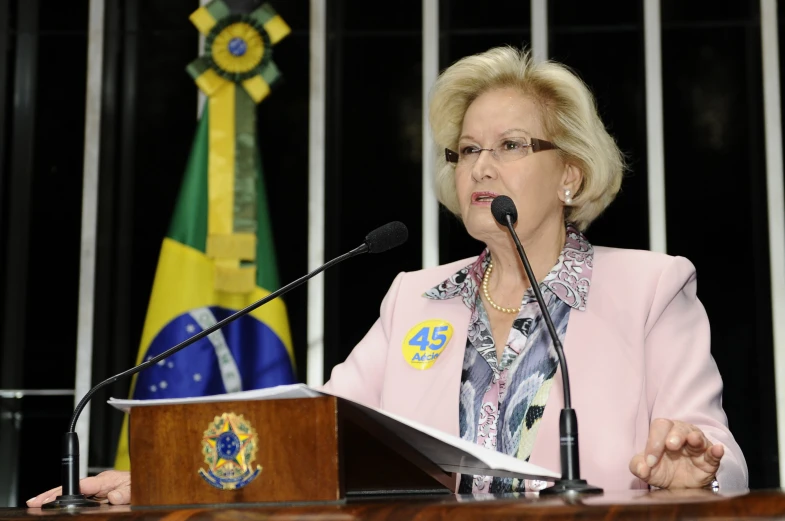 an older woman sitting at a podium and giving a speech