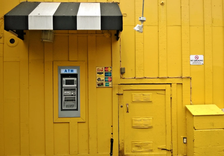 a pay phone in front of a yellow wall