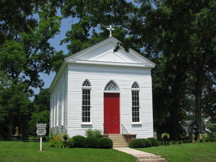 a white church with a red door stands next to a sidewalk