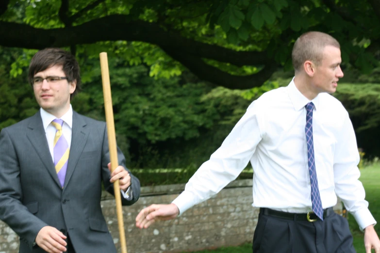 two young men are dressed in business attire and holding a stick