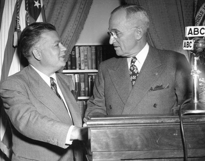 two men standing next to each other, in front of a flag