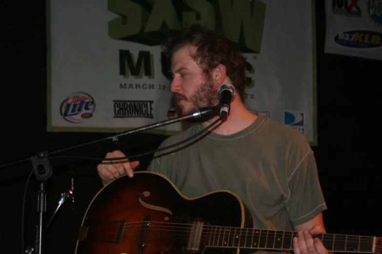 a man holding a guitar while standing at a microphone
