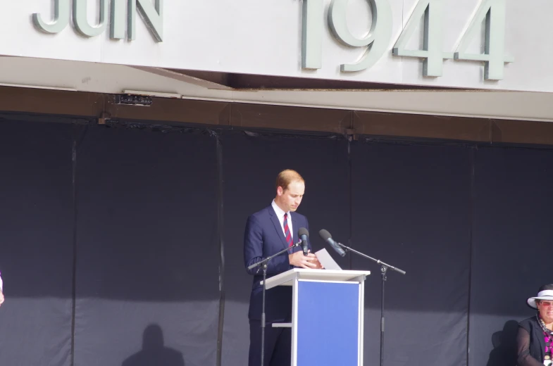 a man in suit speaking from a podium with a microphone