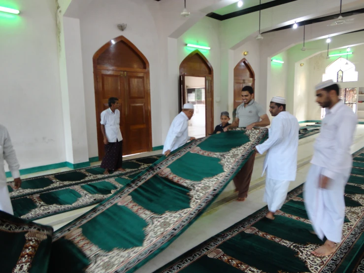 men in traditional dress carry an embroidered rug across the floor