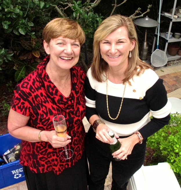 two woman are standing in front of a planter holding drinks