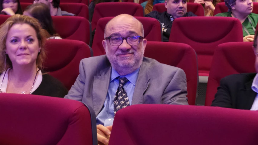 man sitting between women at a conference looking on