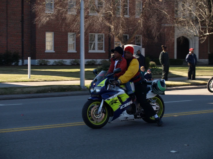 two men riding on the back of a motorcycle down a street