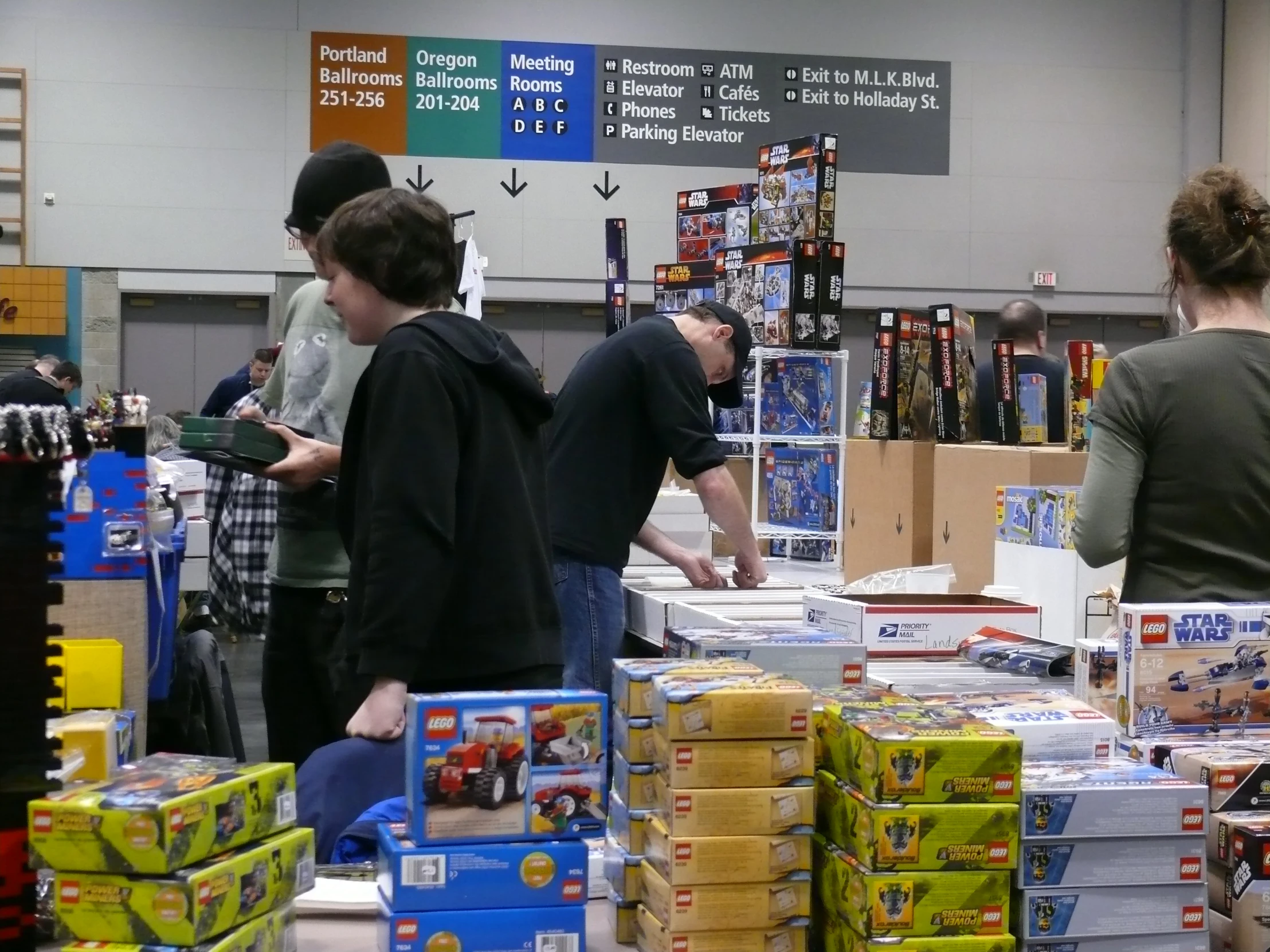 a group of people standing around a table with stacks of toy cars