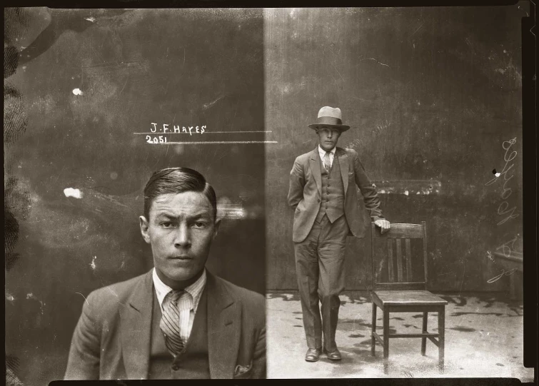 a black and white pograph of a man in a suit sitting next to a chair