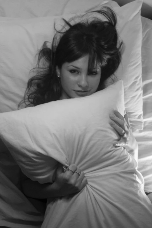 black and white pograph of a young woman lying in bed, hugging pillows
