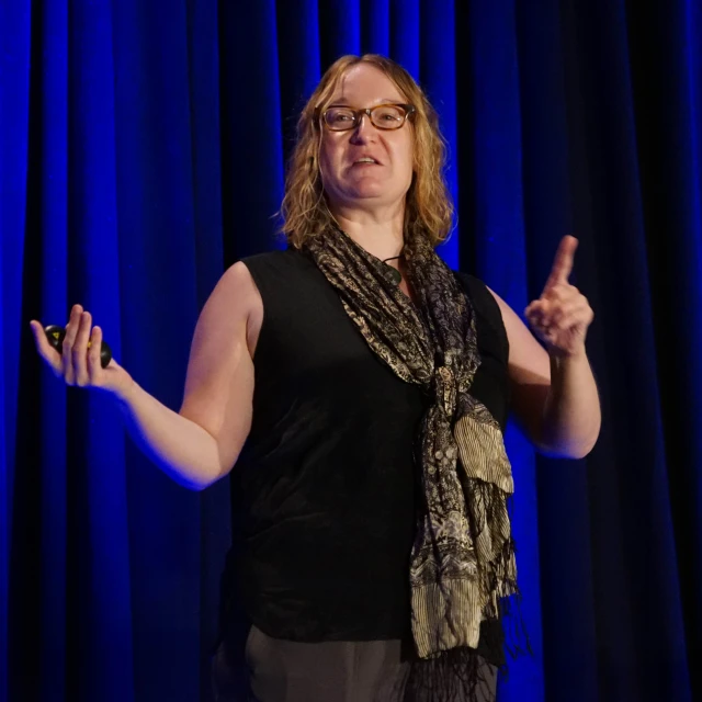 a woman with glasses talking on a stage