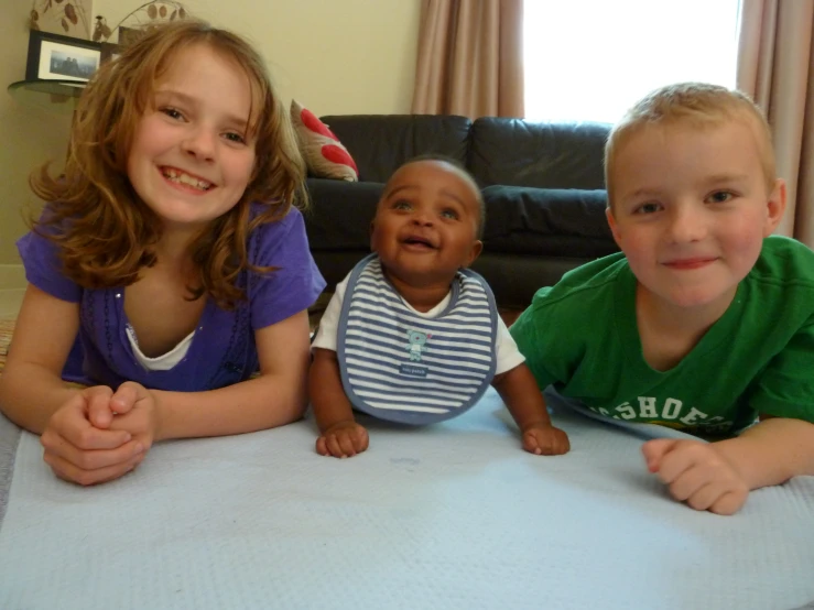 three children are laying on a mattress near a black couch