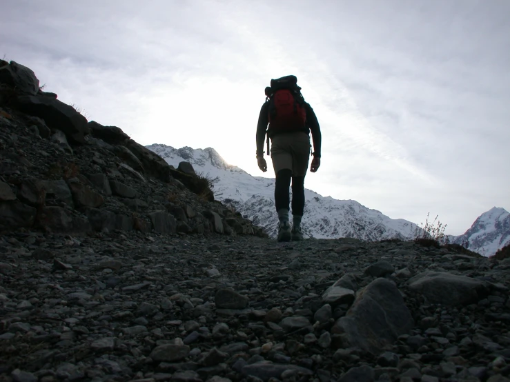 a hiker pauses in the snow near a rocky mountain