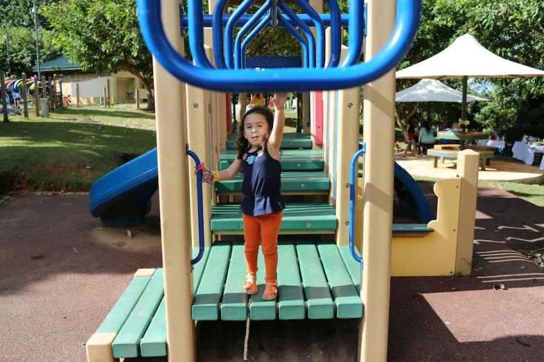 the little girl stands at the bottom of a playground structure