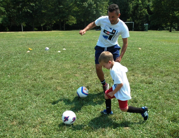 man helping child play soccer on a field