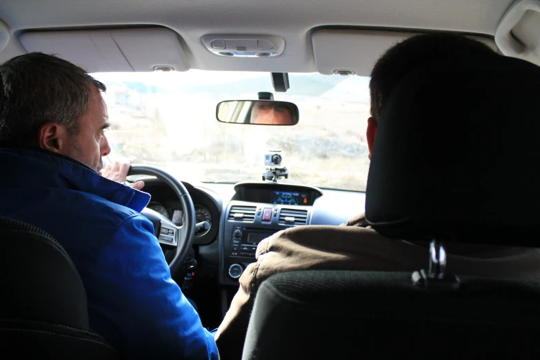 two men sitting in the front of a car, both using their headset