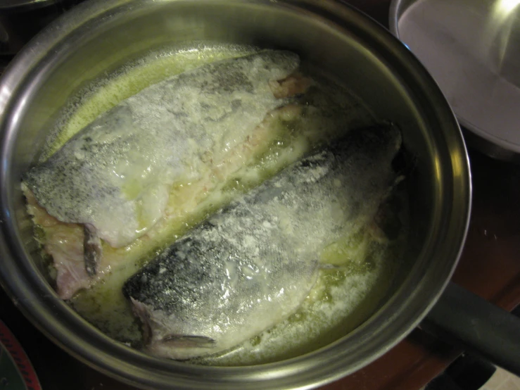 two large fish in an oiled pan on a stove