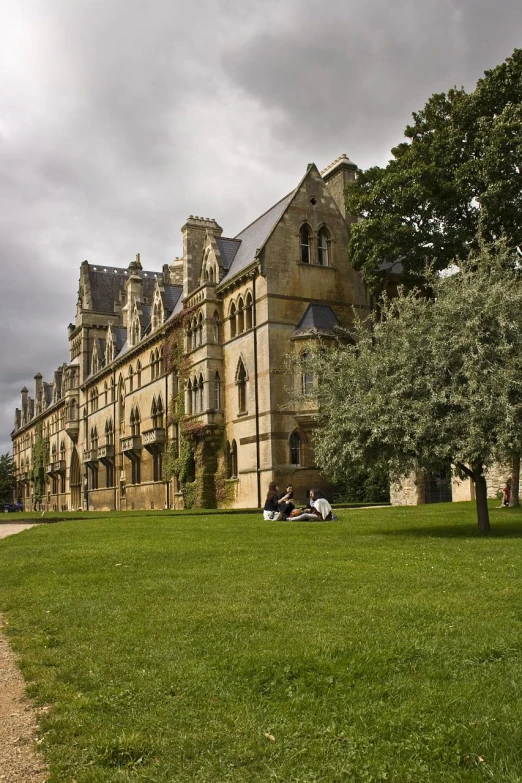 two people relax in the grass on a field below an old building