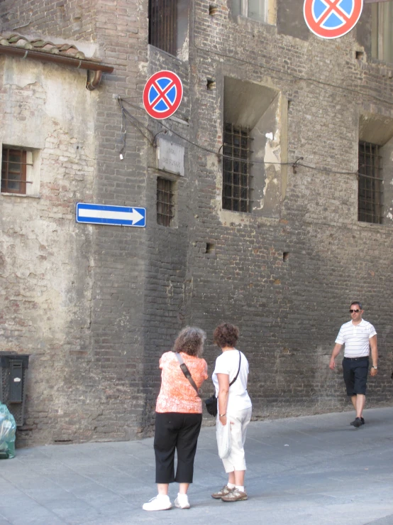 a few people walk down a street beside brick building