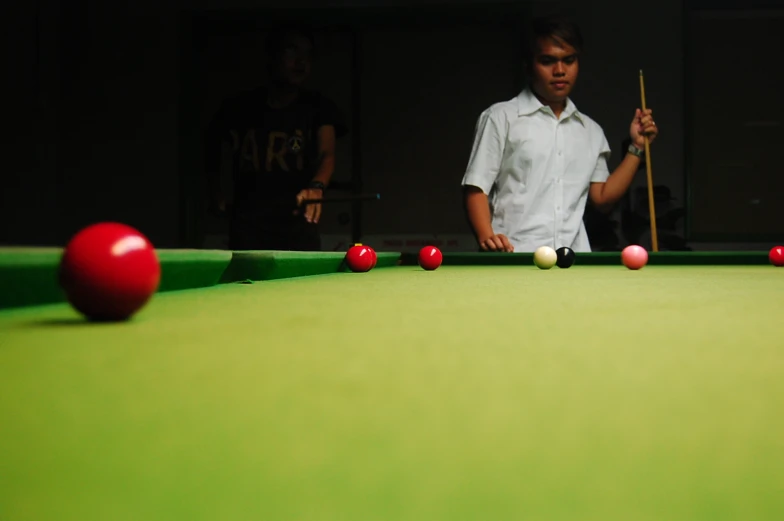 a man standing by a pool table with red balls on it